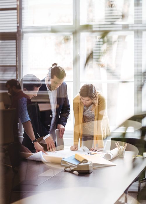 Business people with digital tablet and blueprint on table seen through glass