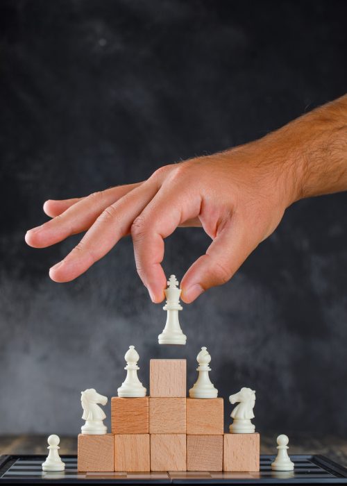 Business success concept with chessboard on wooden and foggy background side view. man placing figure on pyramid of blocks.